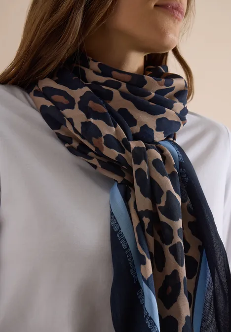 Frau in weißem Shirt trägt einen beigen und blauen Leopardenmuster-Schal um den Hals.