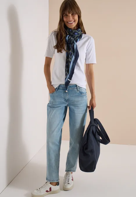 Frau trägt weißes T-Shirt, helle Jeans, karierten Schal und hält eine blaue Tasche.