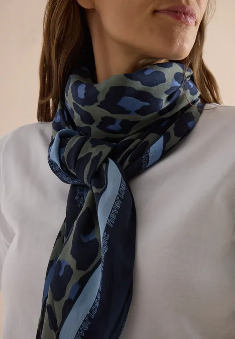 Frau mit weißem Oberteil trägt einen blau-grünen Camouflage-Schal locker um den Hals gebunden.