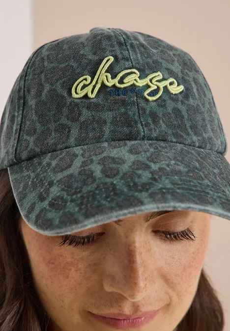 Person mit grün gemustertem Cap mit chase-Logo und Sommersprossen blickt nach unten.