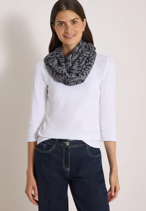Frau in weißem Langarmshirt, dunkler Jeans und grau-schwarzem Loop-Schal.