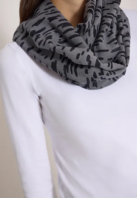 Grauer Schal mit schwarzem Camouflage-Muster über einem weißen Oberteil drapiert.