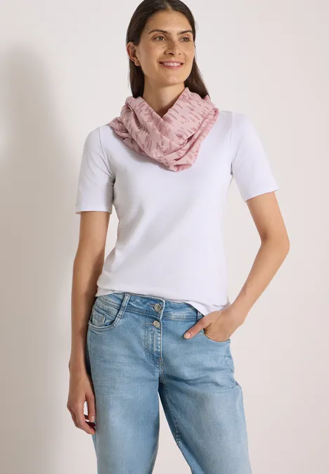 Frau trägt weißes T-Shirt, blaue Jeans und rosa Schal vor hellem Hintergrund.