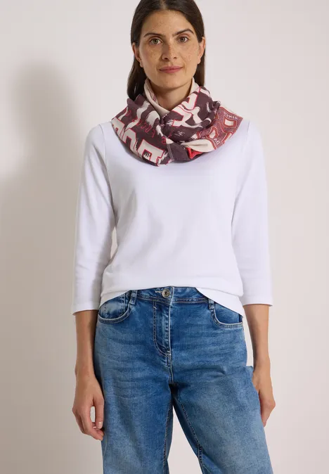 Frau in weißem Langarmshirt, blauen Jeans und gemustertem Loop-Schal.