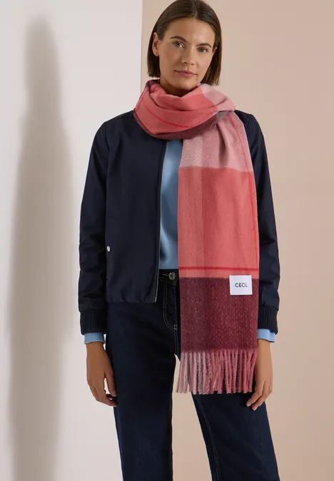 Vrouw in marineblauw jasje, blauwe jeans en roodroze sjaal tegen een lichte achtergrond.