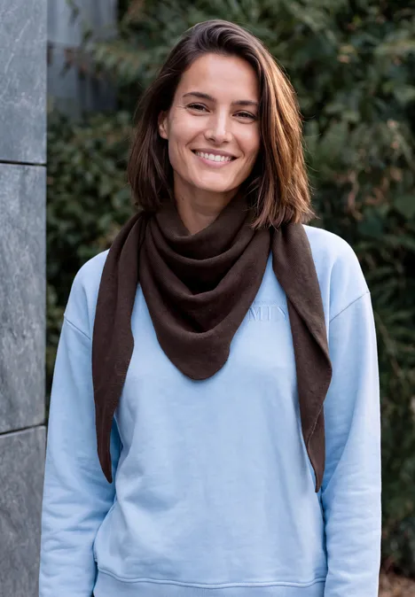 Dreieckstuch in Unifarbe truffle brown Eine lächelnde Frau in blauem Sweatshirt und braunem Schal steht vor einem grünen Hintergrund.