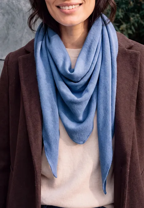 Frau in braunem Mantel, beigem Pullover und blauem, dreieckig drapiertem Schal.