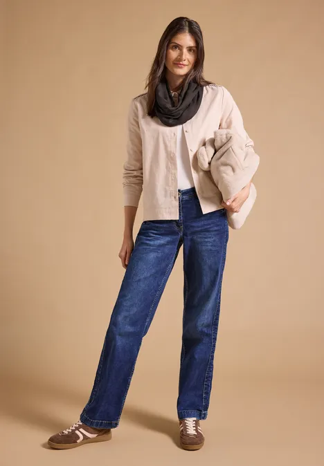 Effen Loop-sjaal truffle brown Vrouw in lichte cardigan, zwarte sjaal, spijkerbroek en loafers voor een neutrale achtergrond.