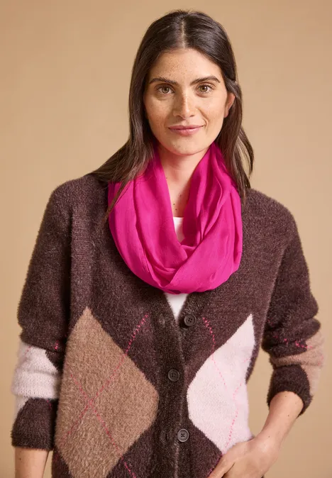 Effen Loop-sjaal pink flash Portret van een glimlachende vrouw in een bruine cardigan met ruitpatroon en roze sjaal voor een beige achtergrond.