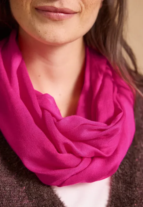 Effen Loop-sjaal pink flash Close-up van een vrouw met een felroze sjaal om de hals en een subtiele glimlach.