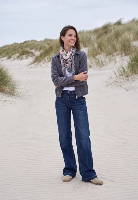 Tuch im Ausbrenner-Look truffle brown Eine lächelnde Frau im Jeans-Outfit und Schal steht entspannt auf einem Dünenstrand mit Gras im Hintergrund.