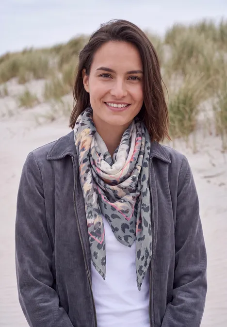 Tuch im Ausbrenner-Look truffle brown Lächelnde Frau mit Schal und Jacke an einem Dünenstrand, grünes Gras im Hintergrund.