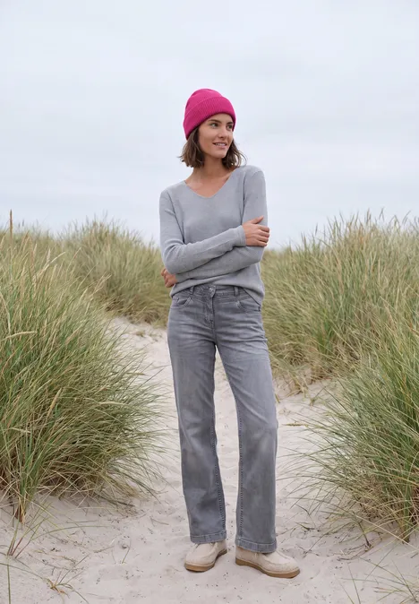 Effen muts pink flash Vrouw met roze muts, grijze trui en broek staat op een zandpad omgeven door duingras.