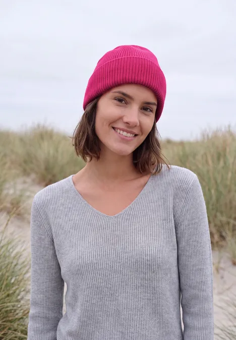 Effen muts pink flash Een lachende vrouw met roze muts en grijze trui voor grasduinen.
