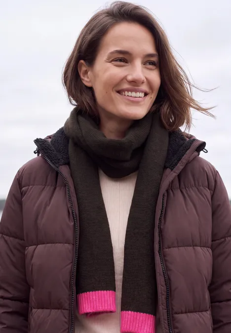 Femme souriante en doudoune marron et écharpe verte à bord rose.