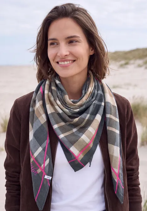 Frau mit kariertem Tuch am Strand mit Dünen im Hintergrund.