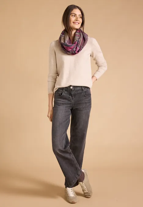 Loop-Schal mit Karomuster mocha brown Frau mit hellem Pullover, dunklen Jeans und buntem Schal steht vor beigem Hintergrund.