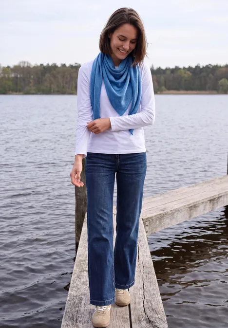 Dreieckstuch in Unifarbe north blue melange Eine Frau in Jeans, langärmeligem Shirt und blauem Schal steht lächelnd auf einem Steg am See.