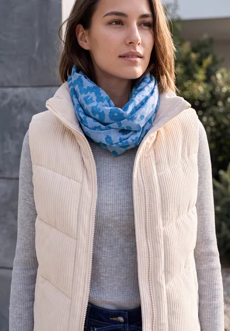 Écharpe Loop avec motif dévoré north blue Frau mit beiger wattierter Weste, grauem Oberteil und blauem Schal im Freien.
