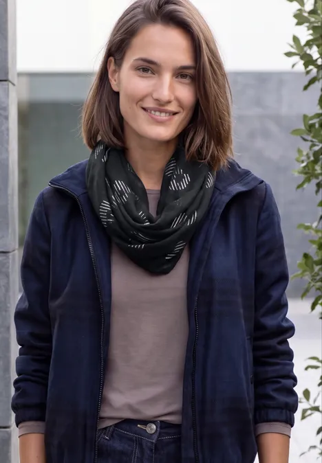 Junge Frau mit kurzem braunem Haar, trägt schwarzen Schal und Jacke, lächelnd vor neutralem Hintergrund