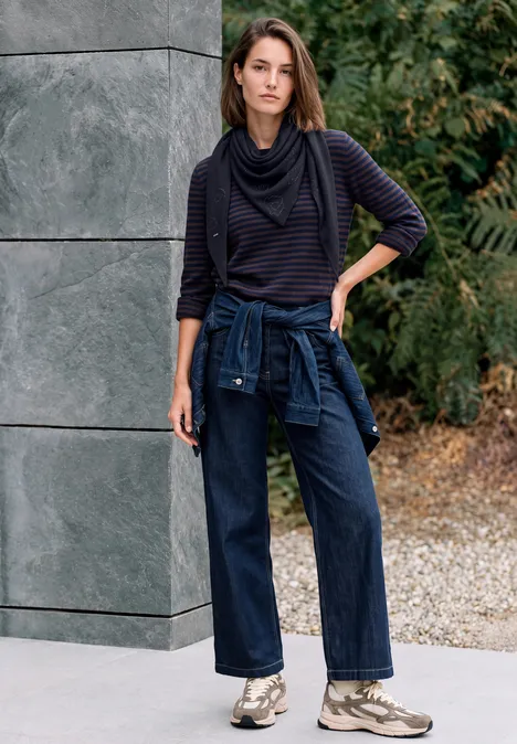 Dreieckstuch mit Glitzerdetails urban dark blue Frau in lässiger Kleidung: gestreiftes Oberteil, weite Jeans, Sneaker, Jacke um die Hüfte, steht vor Mauer und Pflanzen.