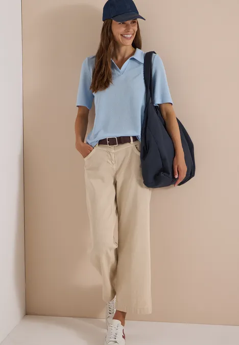 Ceinture Basic à boucle carrée Raisin Frau trägt hellblaues Poloshirt, beige Stoffhose, weiße Sneaker, blaue Cap und große Umhängetasche.