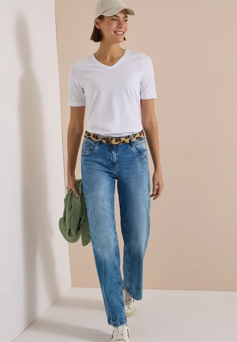 Ceinture en fausse fourrure à motif léopard Natural Leo Print Leather Frau in weißem T-Shirt, Jeans und Cap läuft lächelnd, hält grüne Jacke und trägt Leopardenmuster-Gürtel.