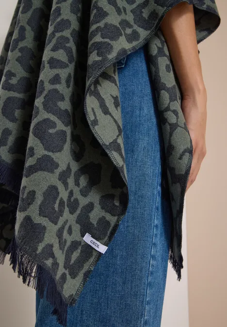 Eine Person trägt einen grün-grauen Poncho mit Leopardenmuster über blauen Jeans.