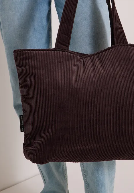Person in blauer Jeans hält eine braune Cord-Tasche fest