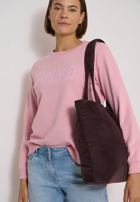 Frau trägt rosa DKNY-Pullover, blaue Jeans und eine große dunkelbraune Schultertasche.