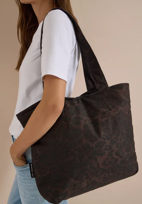 Eine Frau trägt eine große dunkelbraune Leopardenmuster-Shopper-Tasche.