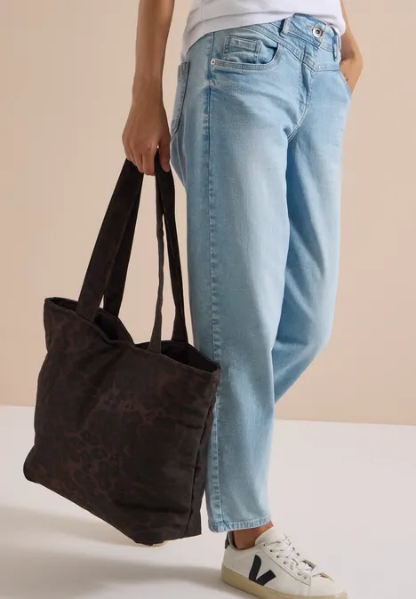 Frau mit blauen Jeans und weißen Sneakern hält eine große schwarze Handtasche.