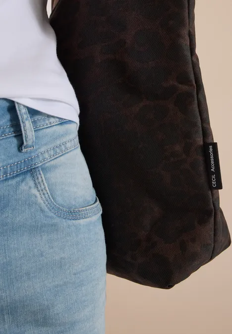 Nahaufnahme einer Person in Jeans und brauner Tasche mit Aufschrift vor neutralem Hintergrund