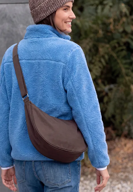 Sac à bandoulière berry red Femme de dos en veste polaire bleue, jean, sac bandoulière marron et bonnet, en extérieur.