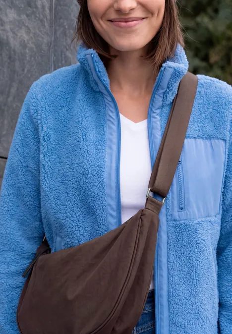 Sac à bandoulière berry red Femme en veste polaire bleu clair, t-shirt blanc et sac bandoulière marron.