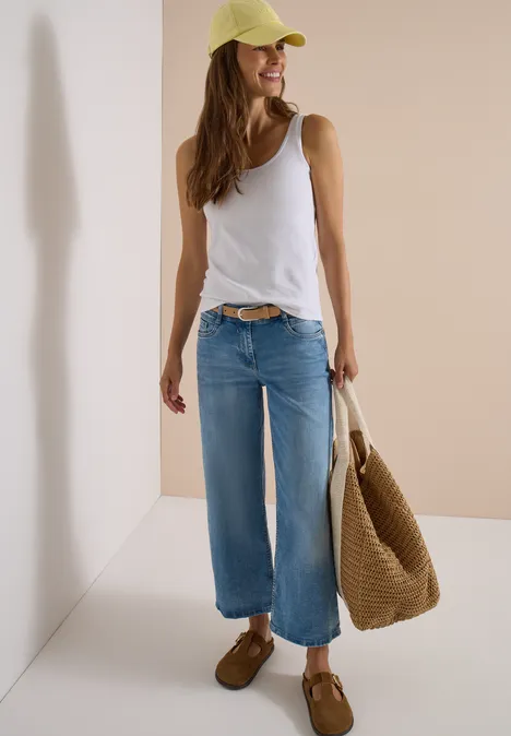 Frau in weißem Top, weitem Jeans, gelber Cap und Basttasche