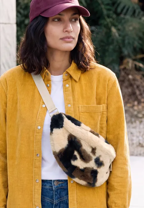 sac à bandoulière pearl beige Femme en casquette bordeaux, veste jaune et sac fourrure beige à taches foncées.