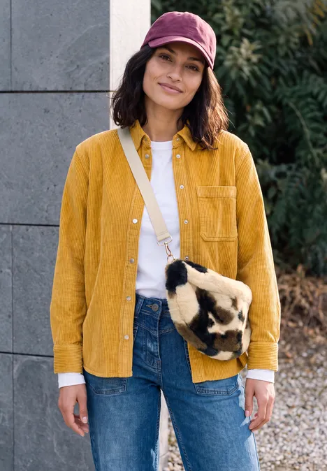 sac à bandoulière pearl beige Femme en chemise en velours jaune, jean et casquette violette, avec sac en fourrure, souriante en extérieur.