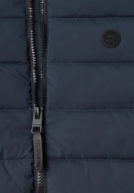 Nahaufnahme einer dunkelblauen, gesteppten Jacke mit Reißverschluss und kleinem, runden Logo.