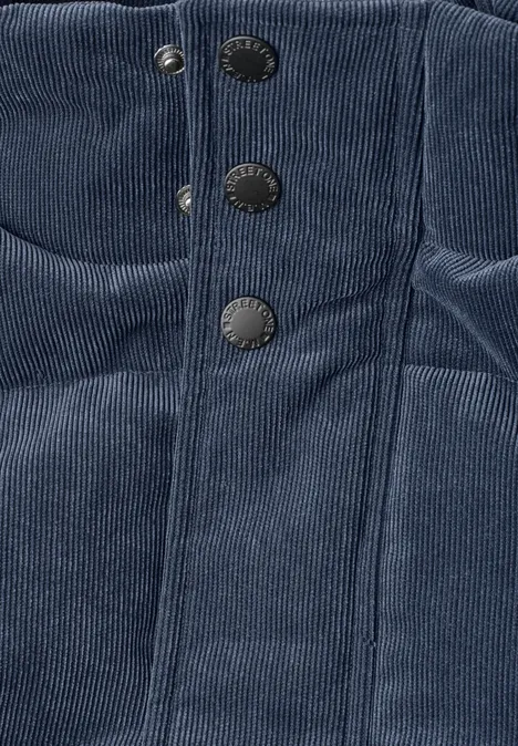 Nahaufnahme eines dunkelblauen Cordstoff-Bekleidungsstücks mit vertikalen Nähten und drei Metall-Druckknöpfen.