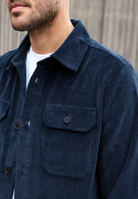 Ein Mann trägt eine dunkelblaue Cordjacke über weißem T-Shirt.