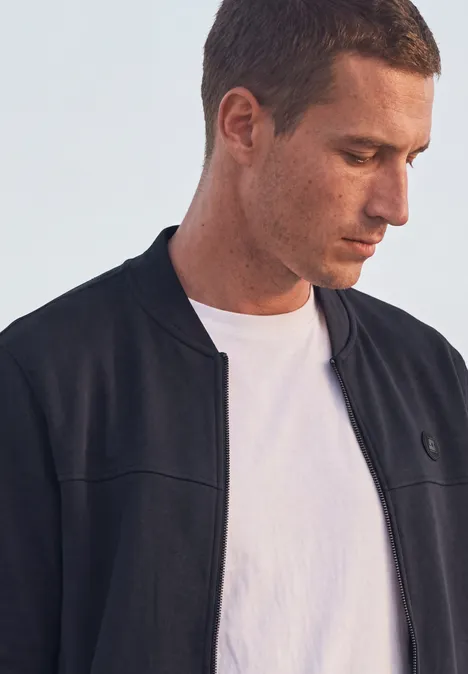 Blouson en piqué double face à fermeture zip dark ink blue Ein junger Mann trägt ein weißes T-Shirt und eine dunkle Jacke und schaut nach unten.