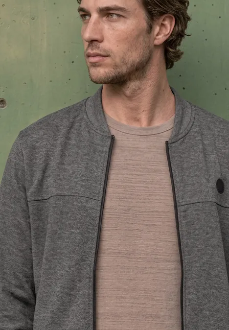 Doubleface Piqué Blouson mit Zipper metal grey melange Ein Mann in braunem T-Shirt und grauer Jacke vor grüner Metallwand.