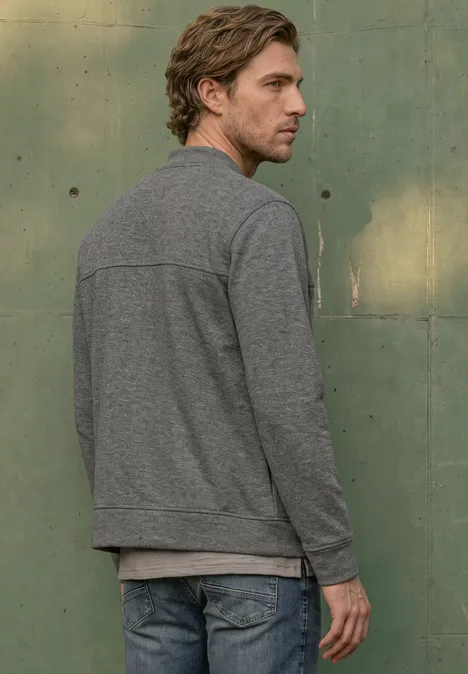 Doubleface Piqué Blouson mit Zipper metal grey melange Mann im grauen Pullover steht vor grünem Hintergrund und blickt über die Schulter