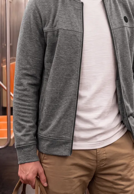 Person in grauer Jacke, weißem T-Shirt und beigen Hosen steht in einer U-Bahn.