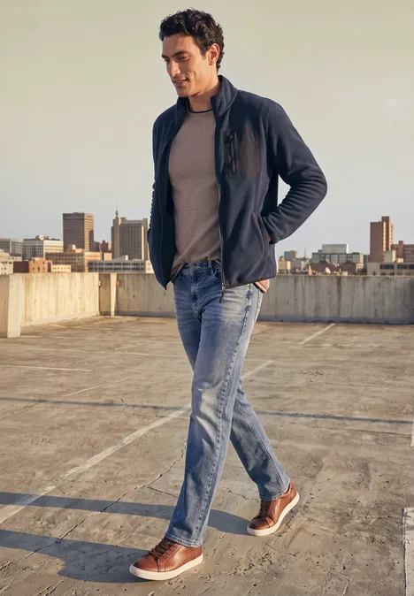 Ein Mann in Jeans, T-Shirt und Jacke läuft über eine leere Dachparkebene bei warmem Licht der Abendsonne.