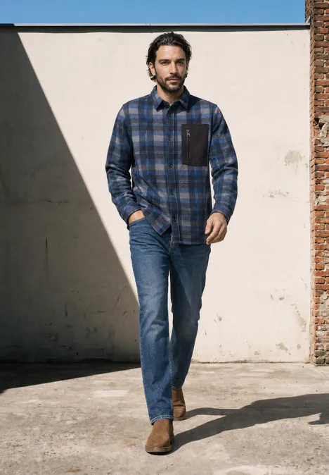 Ein Mann in blau kariertem Hemd, Jeans und braunen Stiefeln geht draußen spazieren.