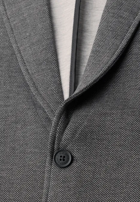 Close-up van een grijs visgraatcolbert met een knoop en een licht T-shirt eronder.