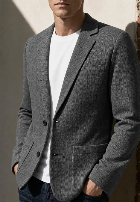 Man draagt grijs colbert met wit T-shirt, handen in de zakken