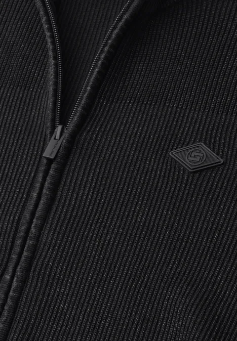 Close-up van een zwarte ribgebreide jas met ritssluiting en klein logo-label.